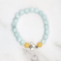 Handmade angelite and honey stone stretch bracelet with bird charm, flat lay on marble
