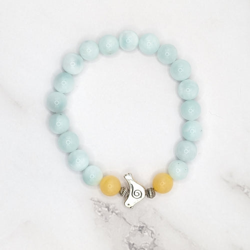 Handmade angelite and honey stone stretch bracelet with bird charm, flat lay on marble