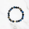 Handmade black line agate stretch bracelet with gold accent beads, flat lay on marble