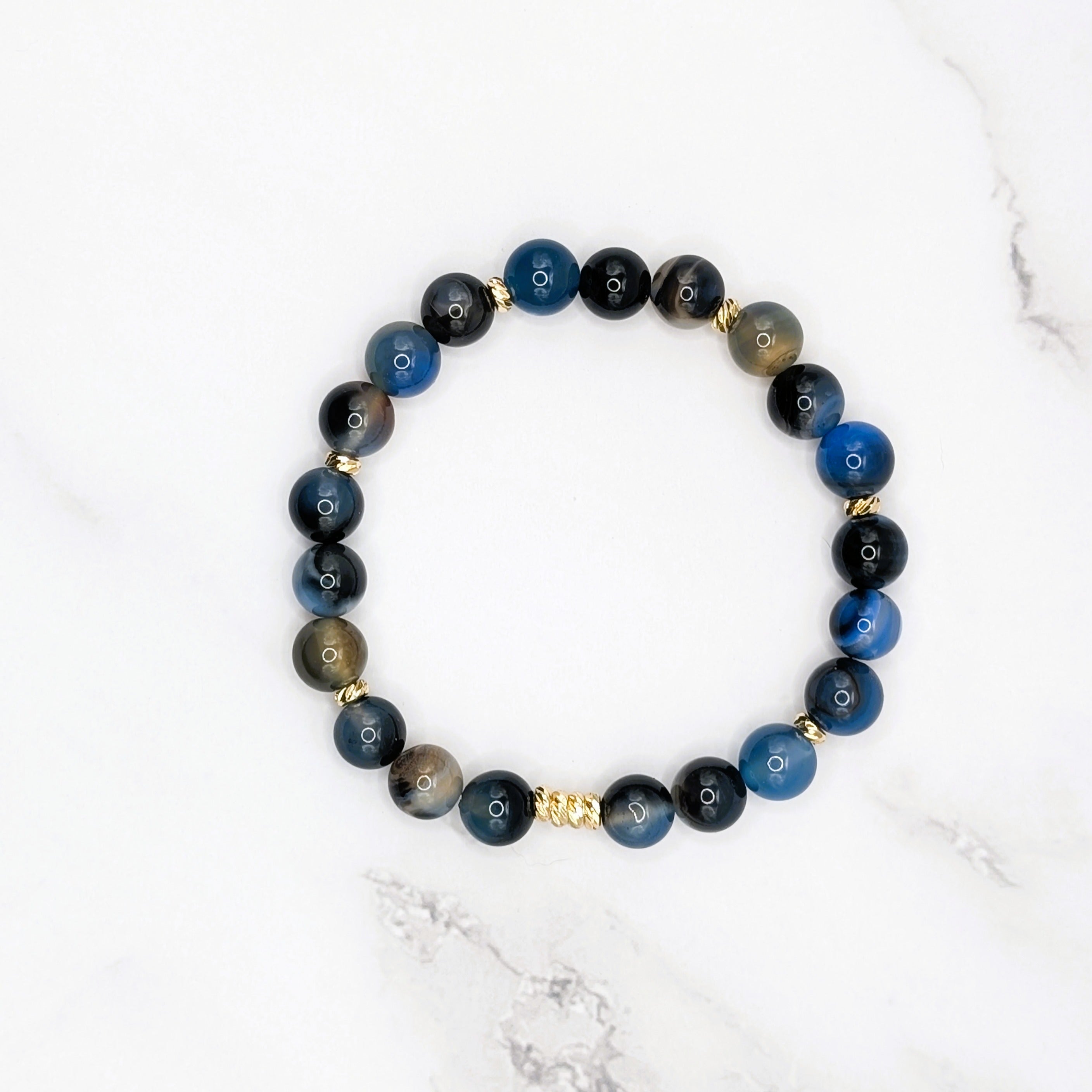 Handmade black line agate stretch bracelet with gold accent beads, flat lay on marble