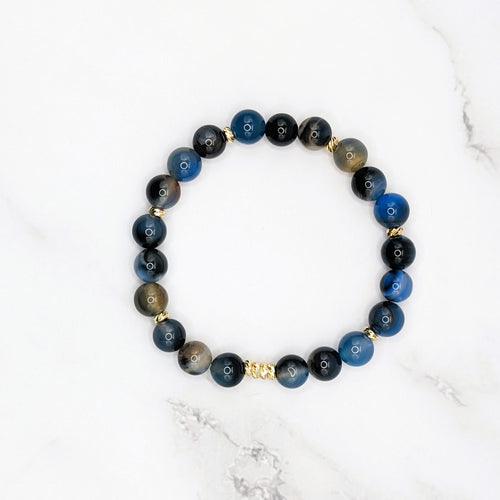 Handmade black line agate stretch bracelet with gold accent beads, flat lay on marble