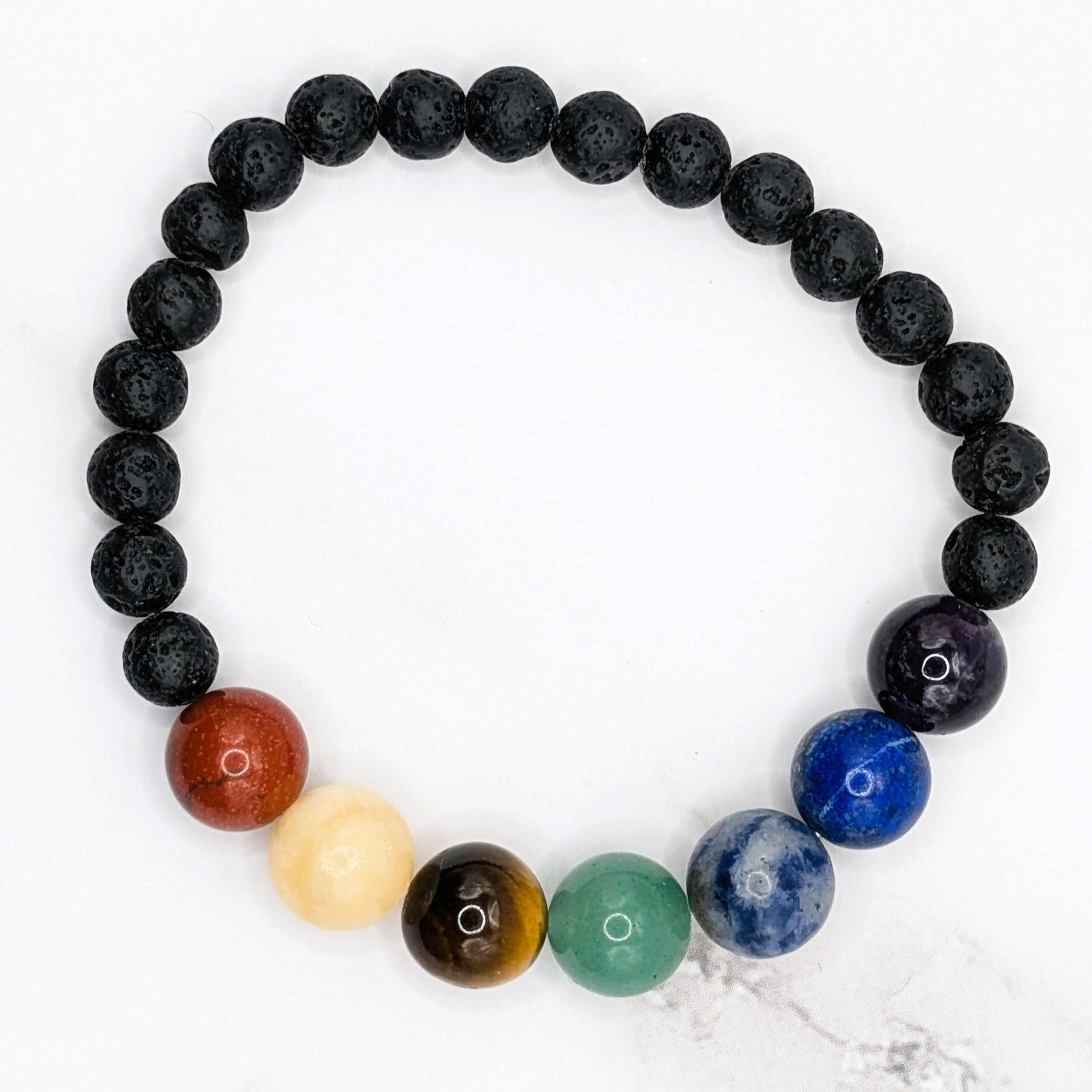 Handmade chakra bead stretch bracelet with lava beads, flat lay on marble