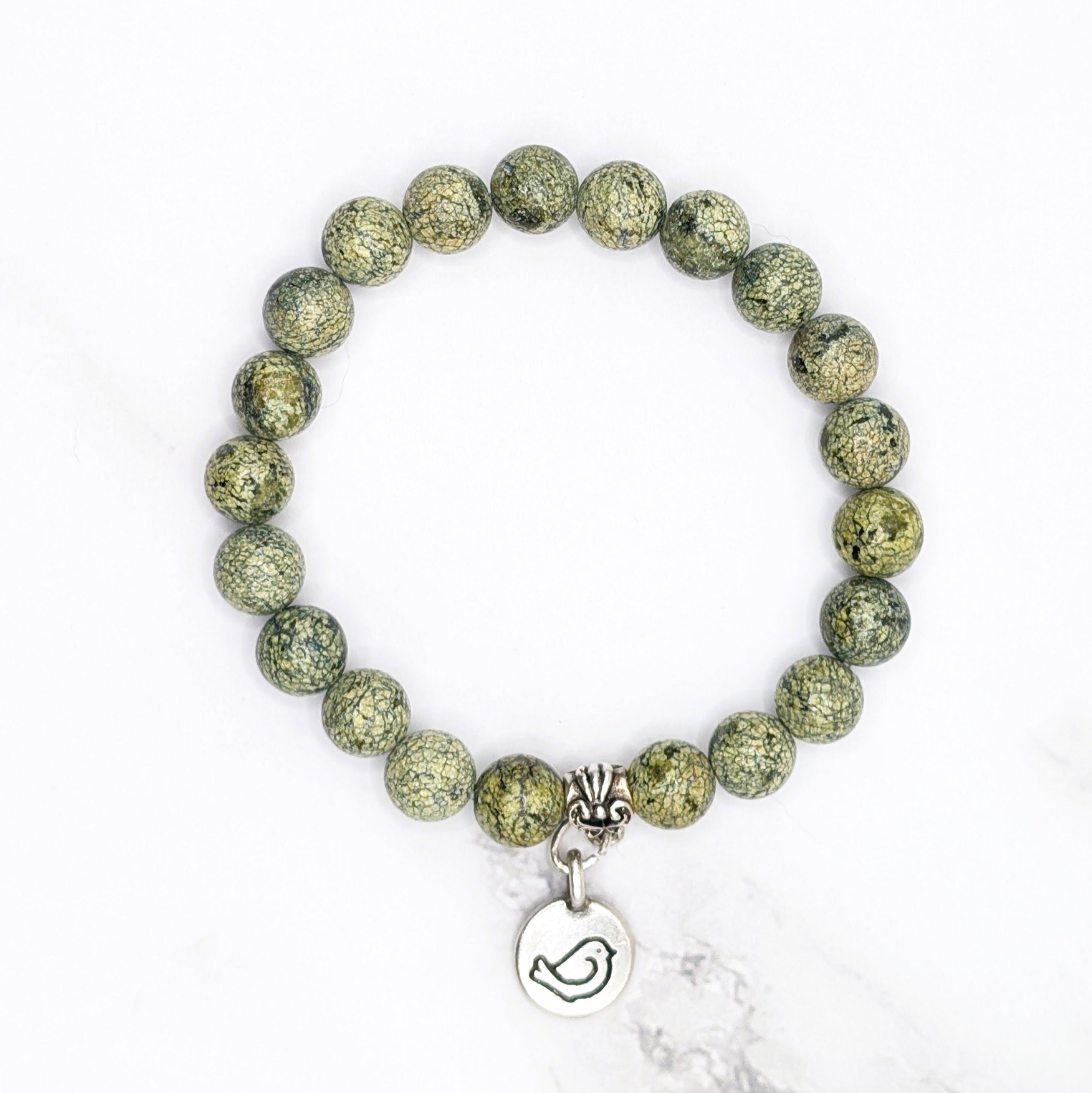 Handmade Russian serpentine stretch bracelet with bird charm, flat lay on marble