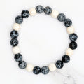 Handmade snowflake obsidian and white howlite stretch bracelet, flat lay on marble