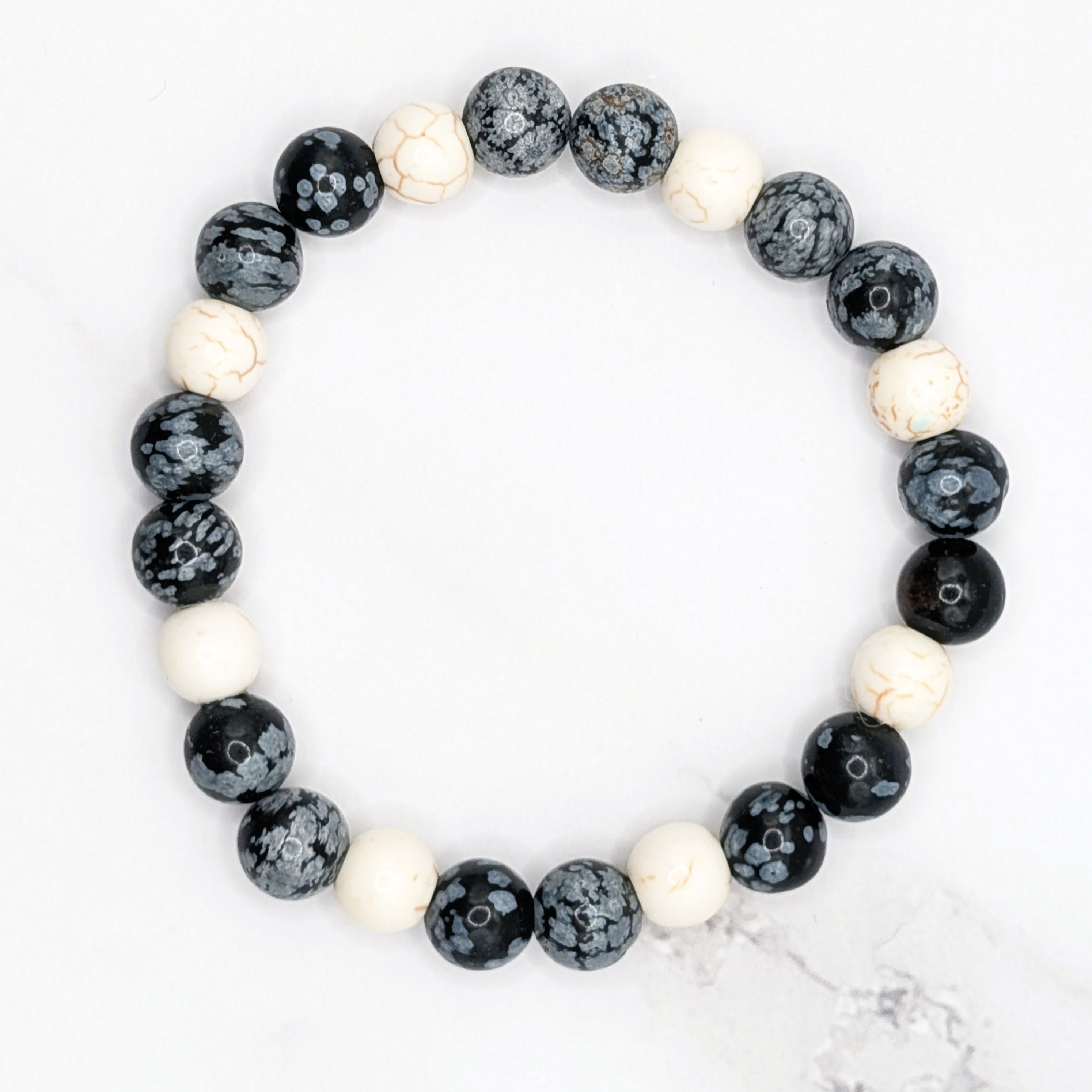 Handmade snowflake obsidian and white howlite stretch bracelet, flat lay on marble